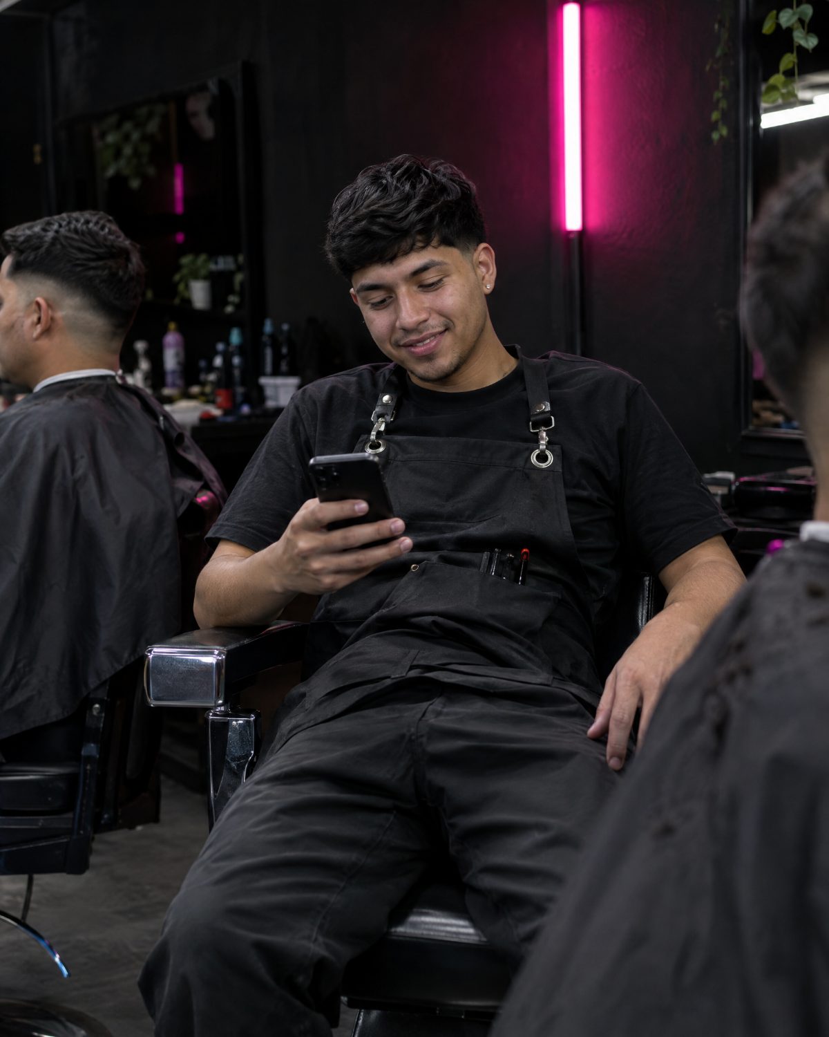 Barbero joven revisa su celular en su barbería, con luz rosada de fondo